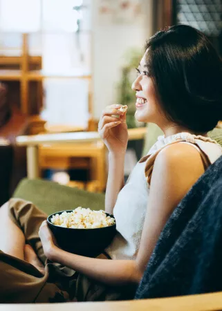 Woman watching TV and eating popcorn on couch