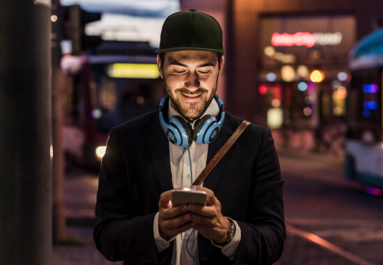 Man on city street smiling at bright ad on phone screen during commute